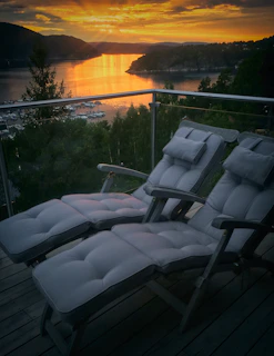 An aluminum outdoor recliner set on a wooden deck overlooking a garden at sunset.