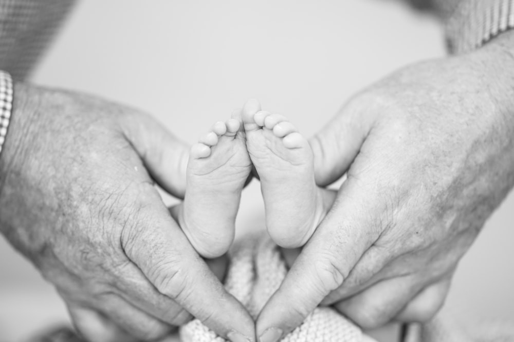 신생아의 발을 안고 있는 사람의 회색조 사진