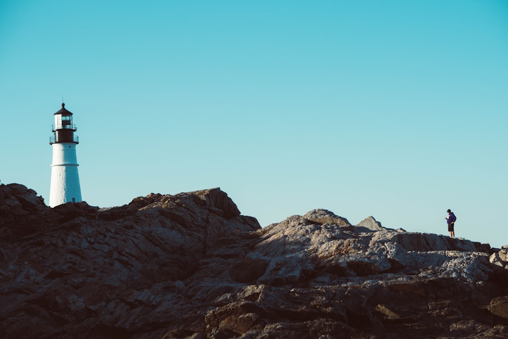 person standing on rock formation in front of lighthouse