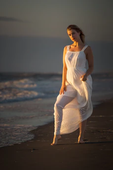 A serene portrait of an Olympian woman standing barefoot on a quiet beach at dawn, the soft light casting gentle shadows that hint at strength and calm.