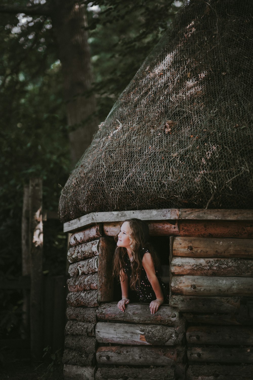 girl in nipa hut window looking upward under trees
