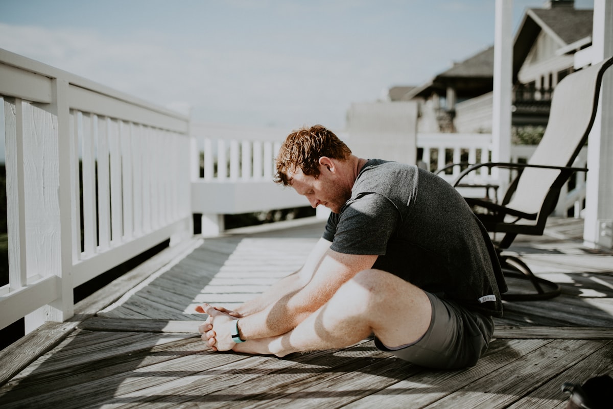 Man doing seated forward stretch on a wooden porch in the morning