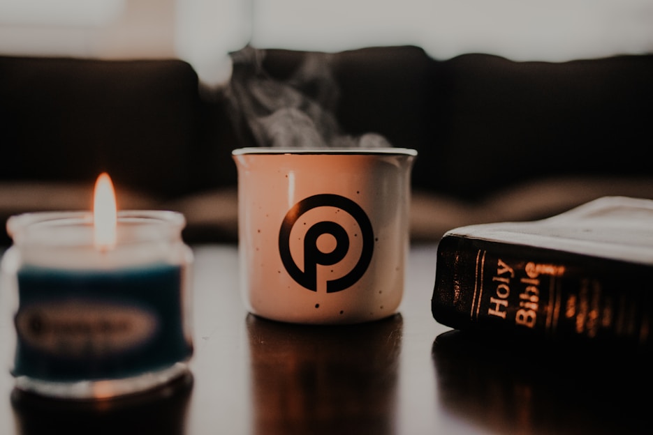 A cozy sweatshirt with a subtle cross design displayed on a wooden table alongside a steaming mug with a scripture quote.