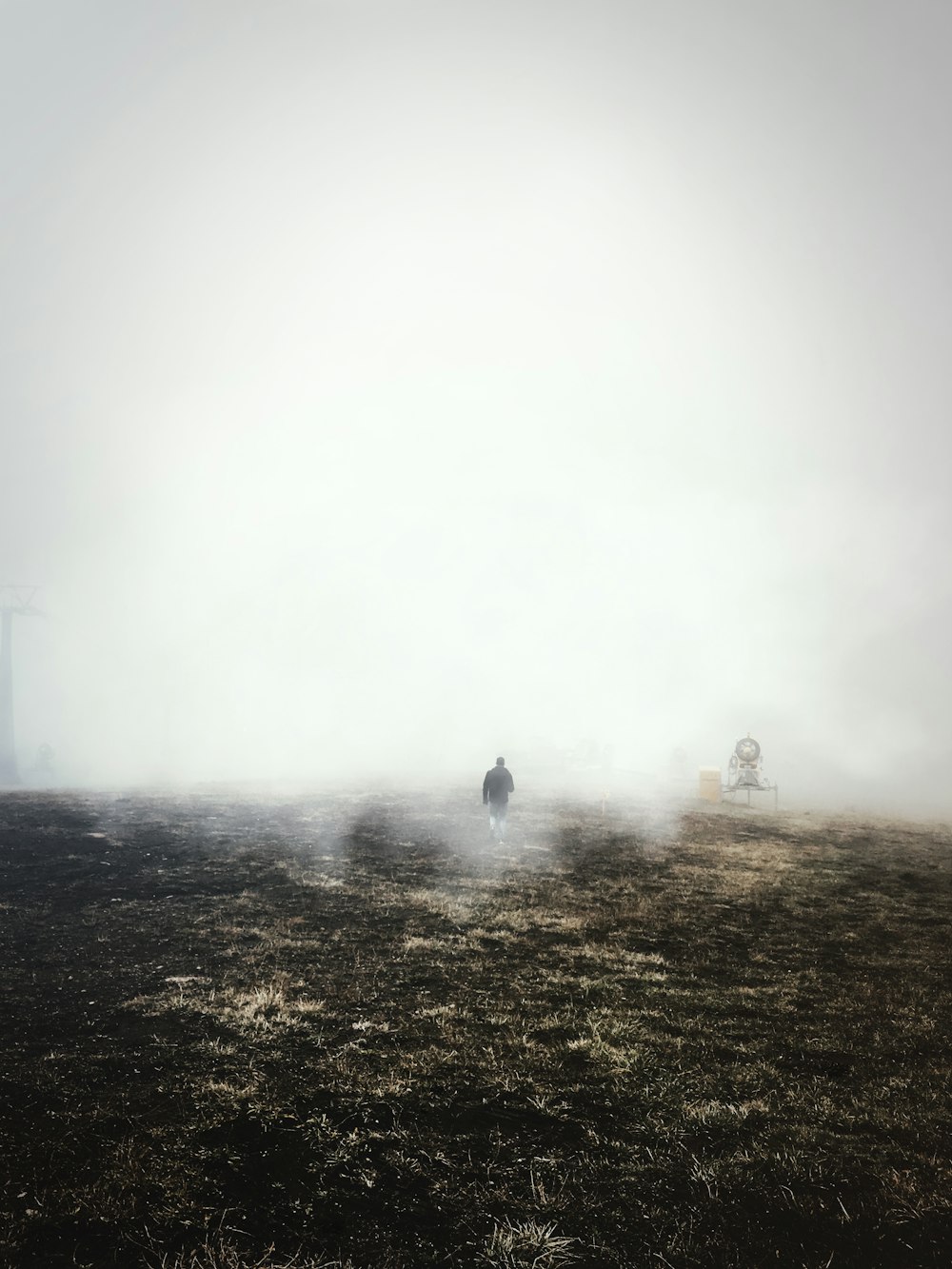 昼間、霧が立ち込める茶色の野原を歩く黒いジャケットの男