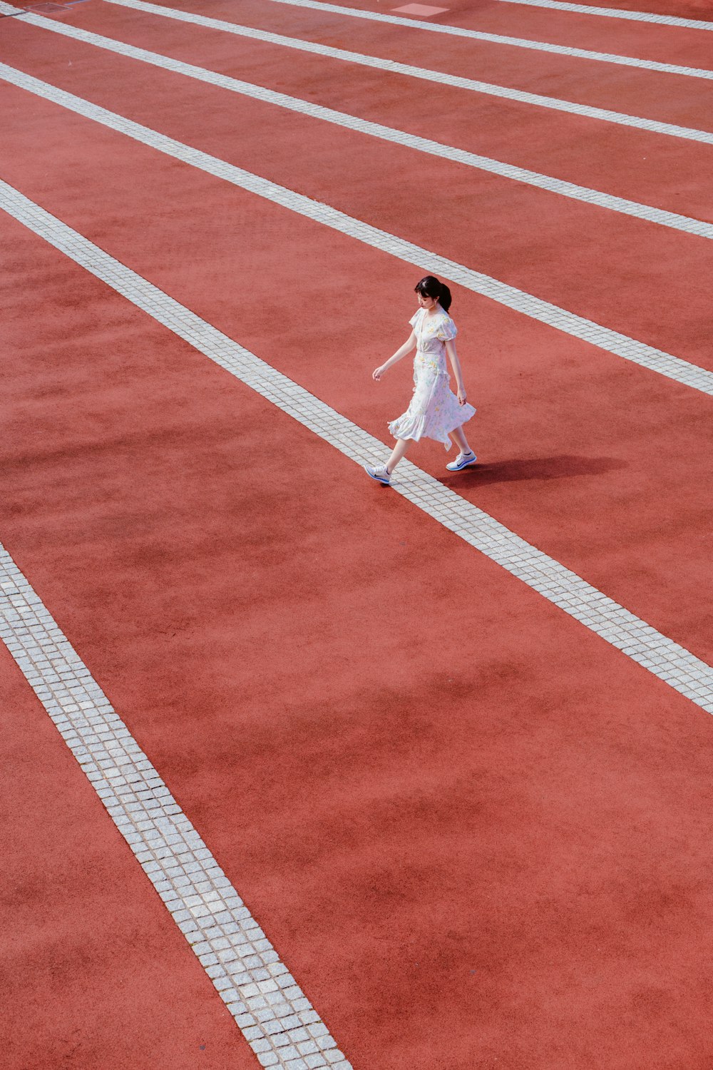 흰 드레스를 입은 여자가 육상 경기를 걷고 있습니다.