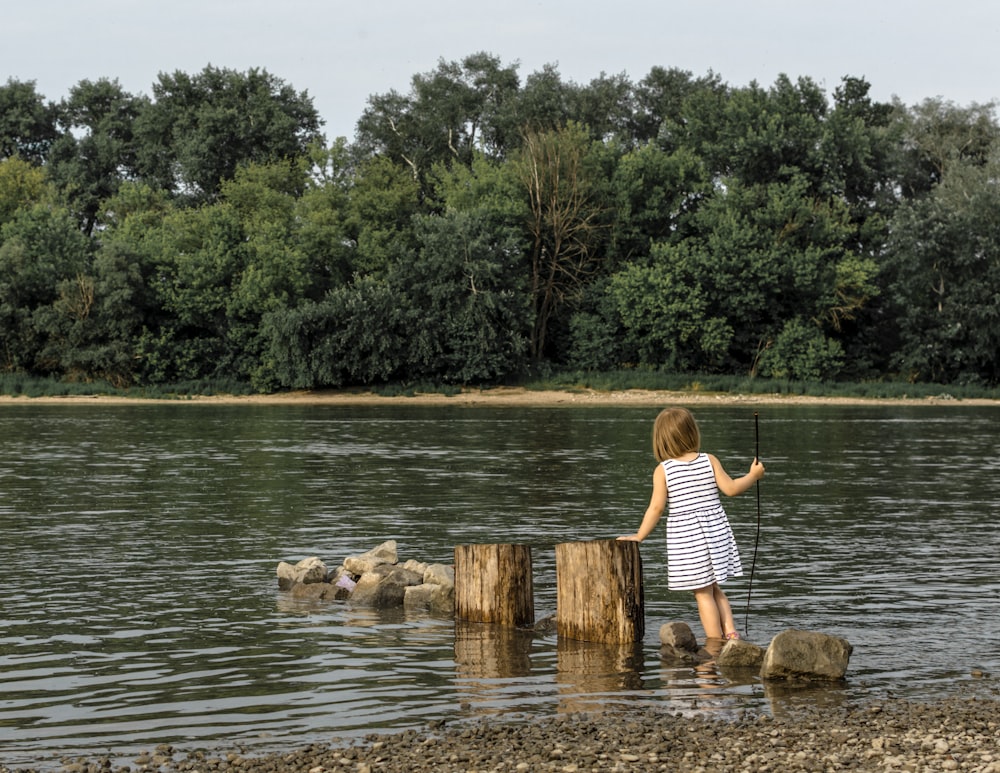 girl standing on gray stone surrounded with body of water