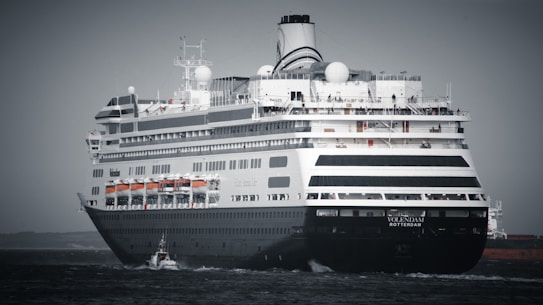 A large cruise ship is sailing on open water, featuring multiple decks and lifeboats along the side. The ship is primarily black and white with distinctive design elements and a name visible at the front.