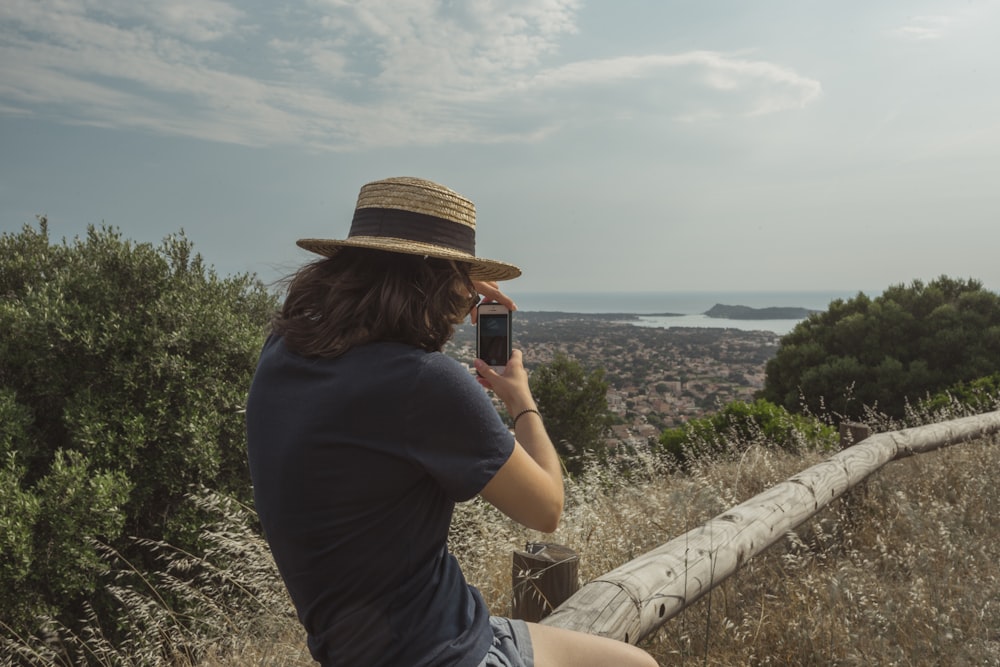 mulher segurando o smartphone tirando fotos de árvores e montanha sob o céu azul claro