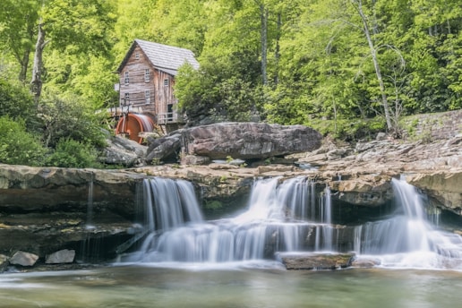 brown waterfalls near house and forest trees during daytime