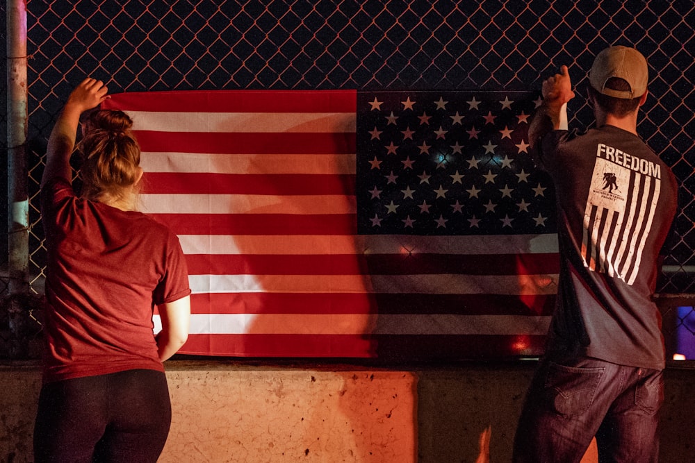 mulher e homem segurando bandeira dos EUA perto de cerca de arame cinza
