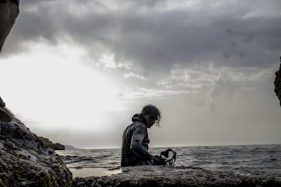 Close-up of a scuba mask resting on a rocky shore with the ocean in the background.