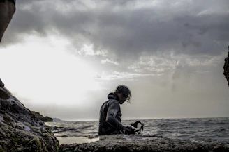 Close-up of a scuba mask resting on a rocky shore with the ocean in the background.
