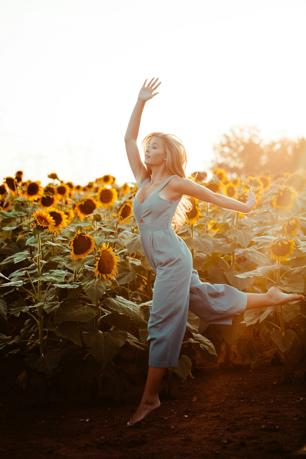 Fotografía de primer plano de la mujer bailando junto al campo de girasoles durante la hora dorada