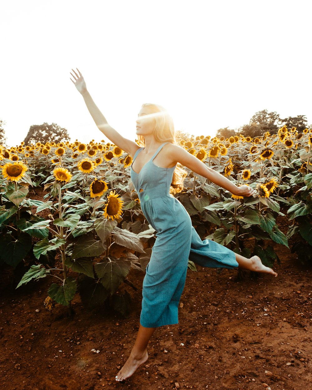 Femme portant des barboteuses vertes sans manches debout et agitant les mains près du jardin de tournesol pendant la journée