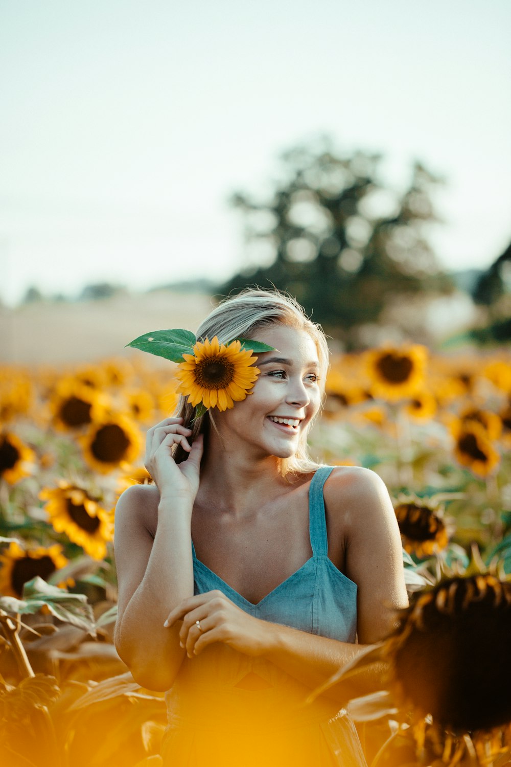 Frau im blauen ärmellosen Kleid mit Sonnenblume im Ohr