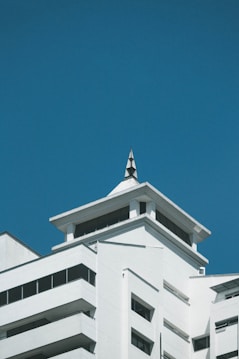 A modern, angular building with multiple levels and a sharp, pointed roof structure set against a clear blue sky. The architecture features clean lines, large windows, and predominantly white exterior walls.
