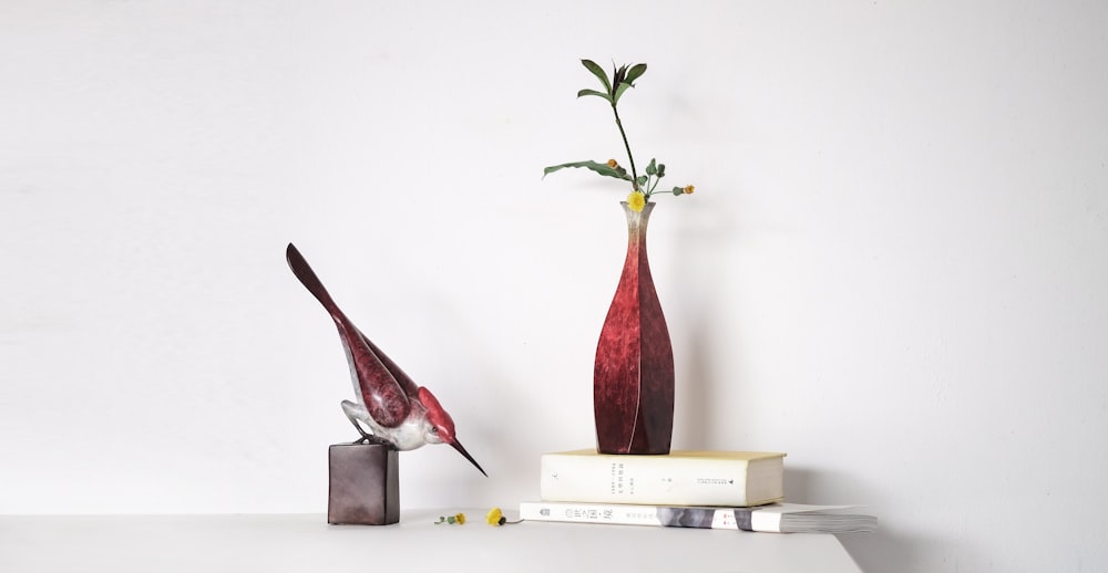 white and maroon bird figurine near red vase