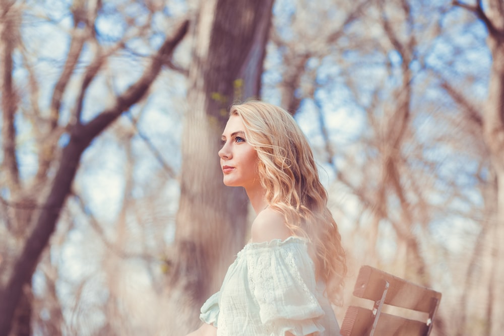 selective focus photo of woman carrying brown bag standing in front of bare trees