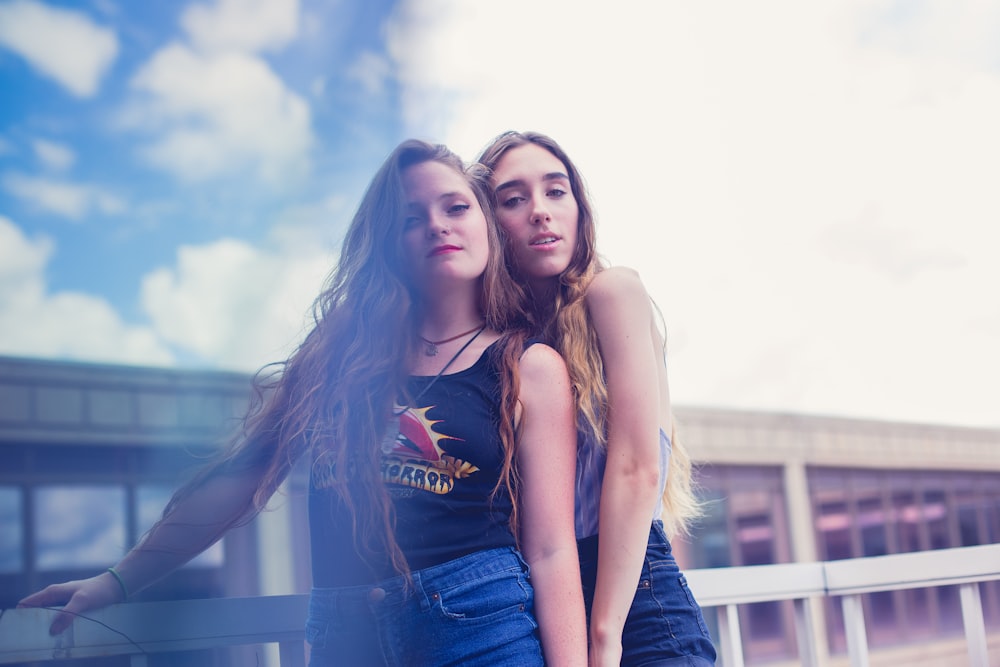 Dos mujeres de pie junto a barandillas de metal blanco bajo el cielo azul y blanco durante el día