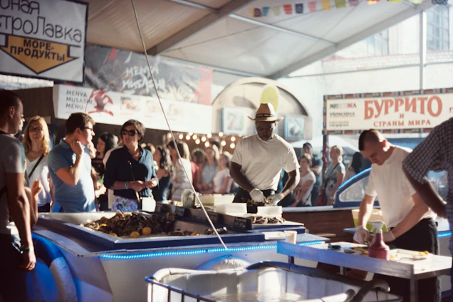 A vibrant festival scene showing local fishermen and chefs preparing fresh seafood together by the shore.