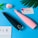 Two electronic beauty devices, one black and one pink, are placed diagonally on a blue surface. Nearby, a delicate pink and white artificial flower, a card with floral designs containing text, and a partially visible page with the word 'VOLK' are positioned.