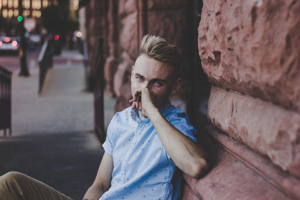 man wearing blue crew-neck sitting near the stone building