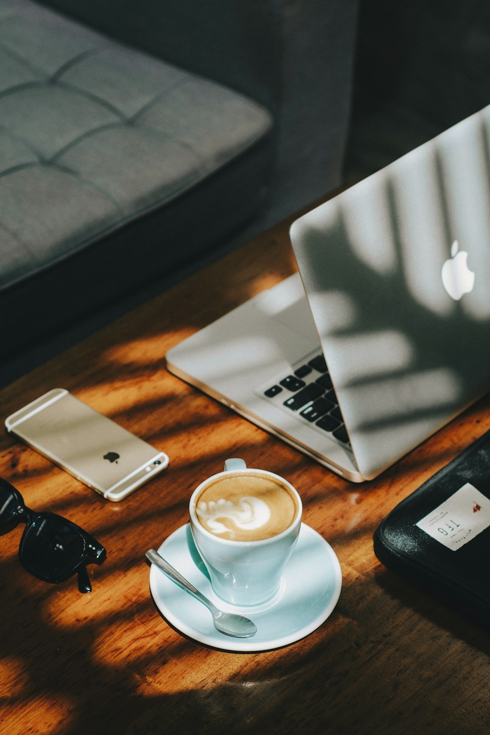 cappuccino in white ceramic cup with saucer beside gold iPhone 6s and laptop