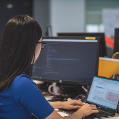 woman using black laptop computer near turned on flat screen computer monitor