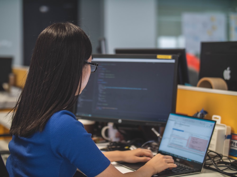 woman using black laptop computer near turned on flat screen computer monitor