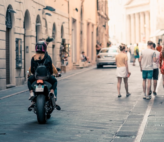 two person riding motorcycle leading towards building at daytime in Assisi Italy