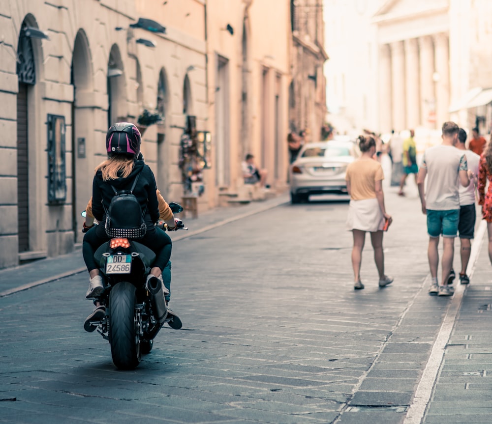 two person riding motorcycle leading towards building at daytime