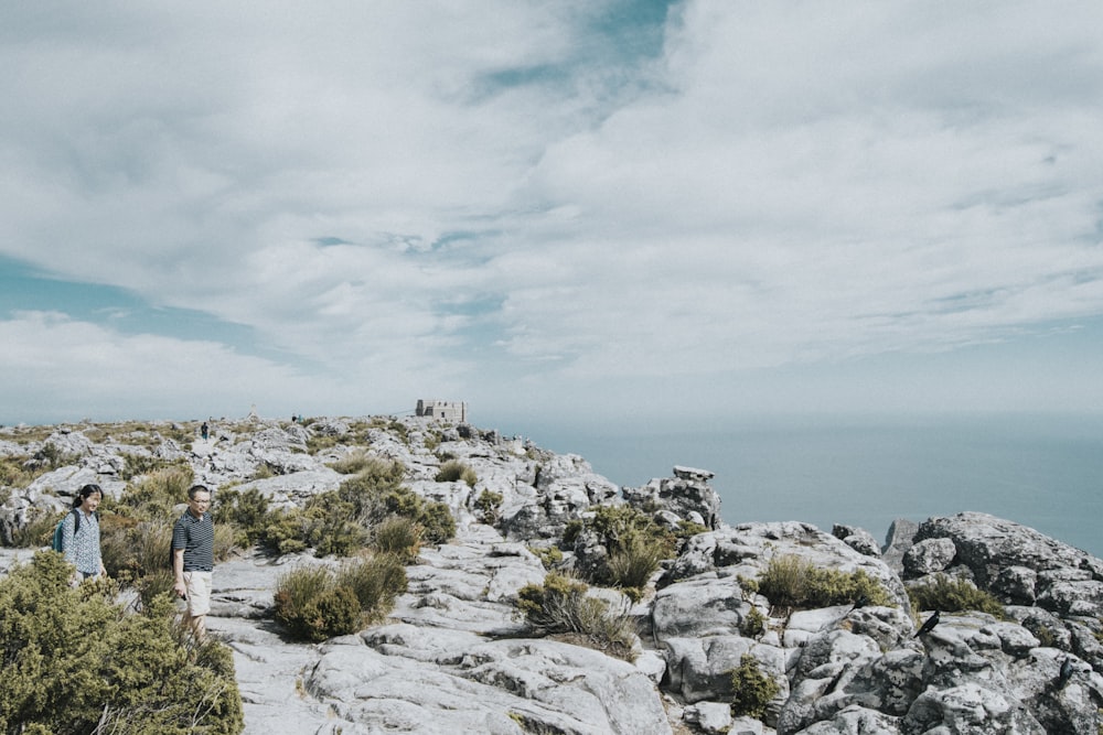 two people standing near grass on grey stone mountain during daytime