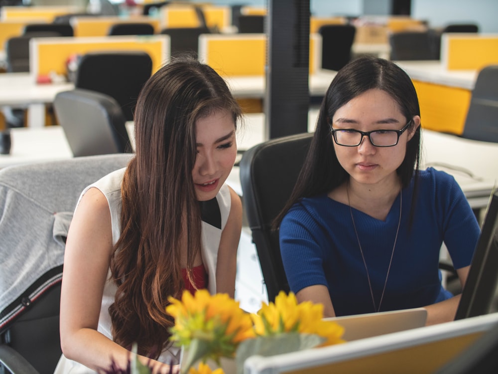 two sitting woman looking at silver laptop computer