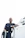 Technician in navy blue uniform pressure washing a rooftop residential water tank under clear sky.