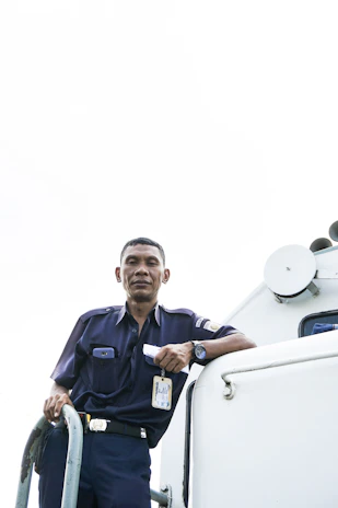 A confident woman in a navy blue uniform directing freight trucks under a clear sky.