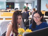 two women smiling in front of computer monitor