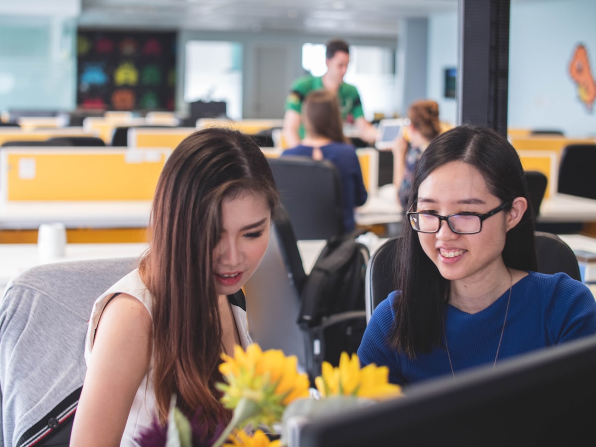 Two Asian women professionals collaborating at a computer in a modern office