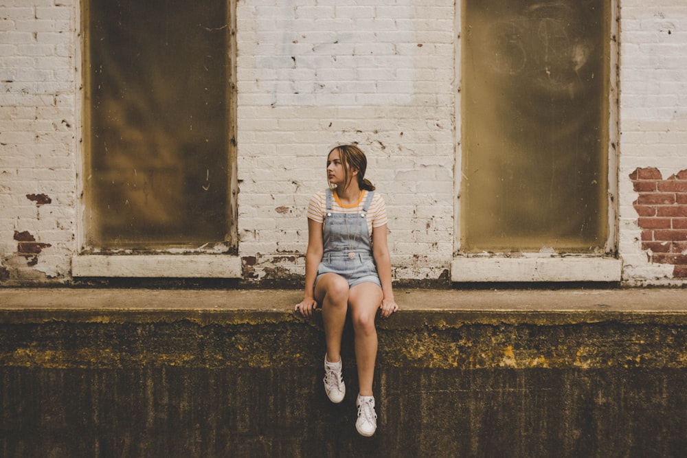 woman wearing overalls sitting on gray concrete surface