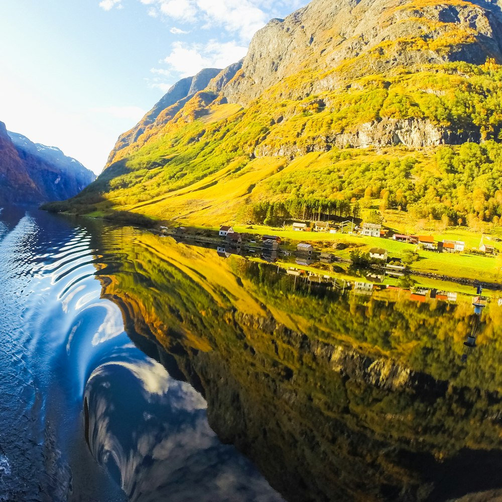 houses near mountain beside lake under blue and white skies