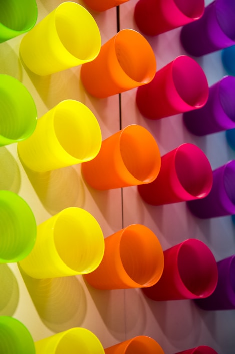 A vibrant display of colorful ceramic cups in various sizes arranged neatly on a shelf.