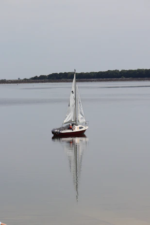Sailing boat cutting through calm waters with reflections of the hull in the sea.