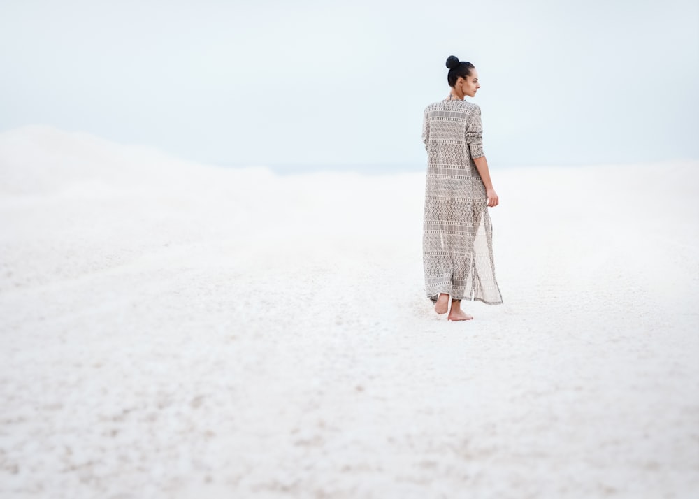 회색 드레스를 입은 여자가 모래 위를 걷고 있다.