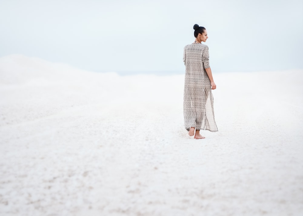 Mujer en vestido gris caminando sobre la arena