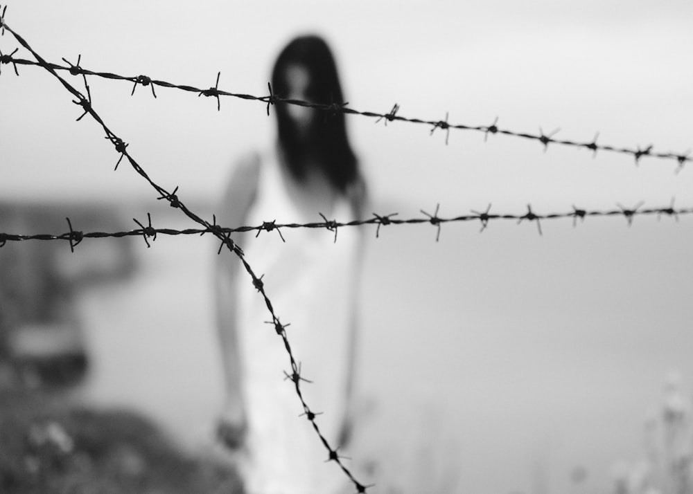 Femme debout sur le rivage près d’une clôture de fil de fer barbelé