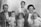 A vintage black-and-white photograph depicting a family gathered closely. An adult man in a suit and a woman with short hair are seated. Between them and in front of them are four small children. The image shows signs of wear with visible creases and marks, suggesting it is quite old.