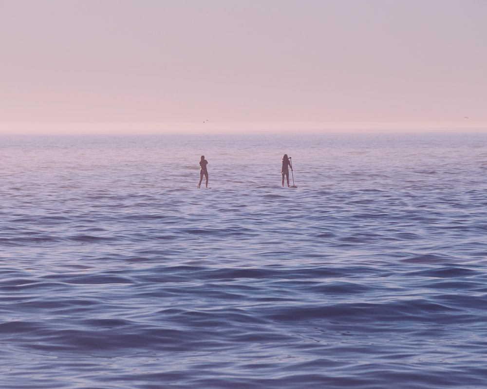 zwei Personen stehen bei Sonnenaufgang auf dem Surfbrett auf dem Meer