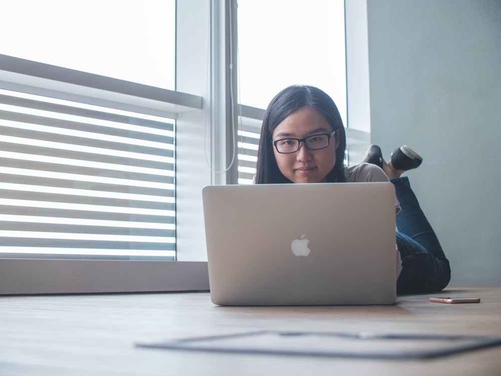 透明なガラス窓のそばで銀色のMacBookを使う女性