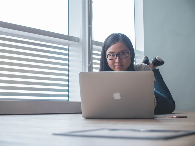 femme utilisant un MacBook argenté à côté d’une fenêtre en v