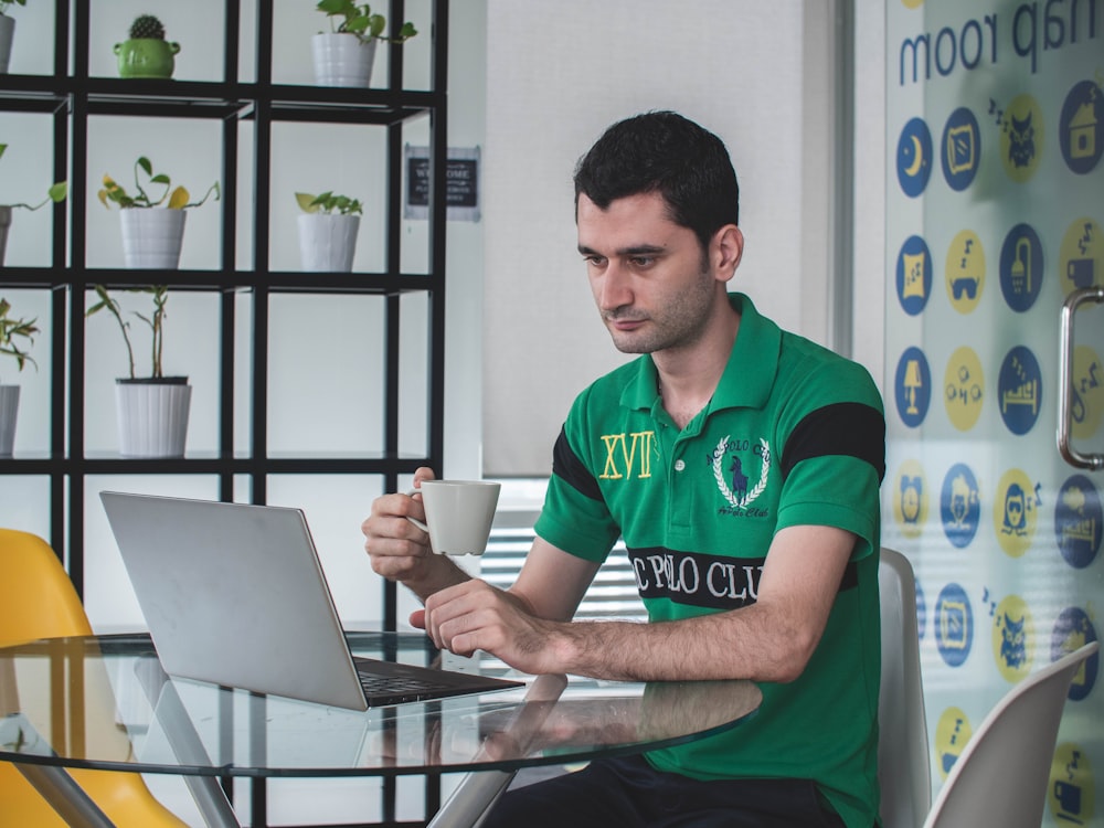 man using laptop computer while holding teacup