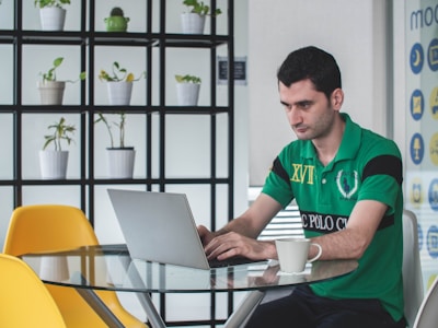 man sitting on gray metal chair while using gray laptop computer